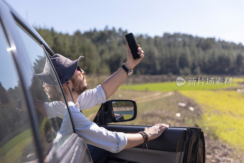 开车旅行时，一名男子一边自拍一边用智能手机发送信息