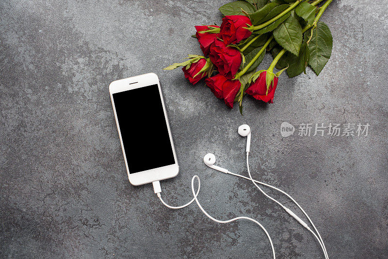 俯视图手机模板和耳机与玫瑰在黑暗的纹理背景与复制空间