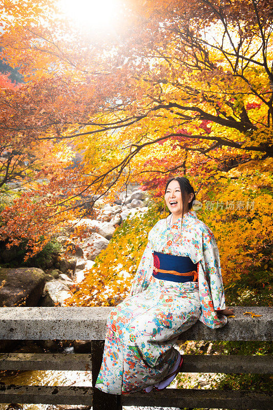 穿着和服的日本女孩和秋天的枫叶坐在桥的栏杆上