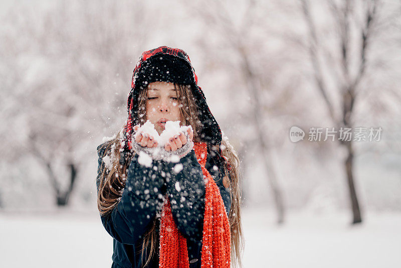 一个年轻的女人在冬天的森林里吹雪