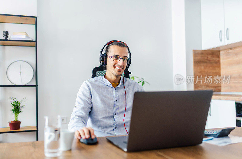 一个商人在他的笔记本电脑上远程工作的肖像。戴着耳机的男人打视频电话。