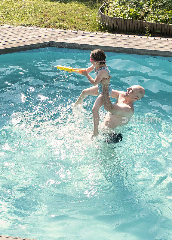 白人家庭，在室外游泳池游泳，父亲与他的女儿和泼水玩。在乡村的室外游泳池里游泳，在一个夏日。