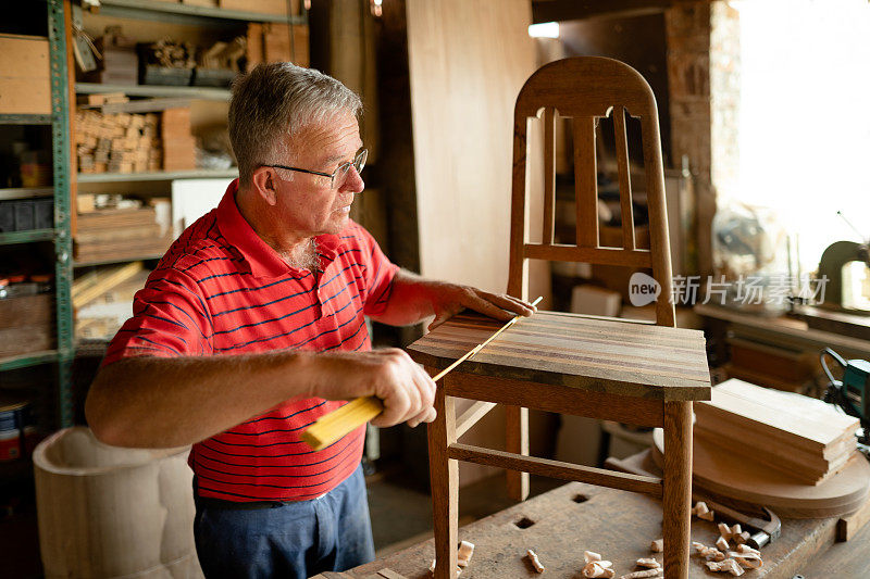 一名年长的男子在他的木工店的工作台上测量一把椅子