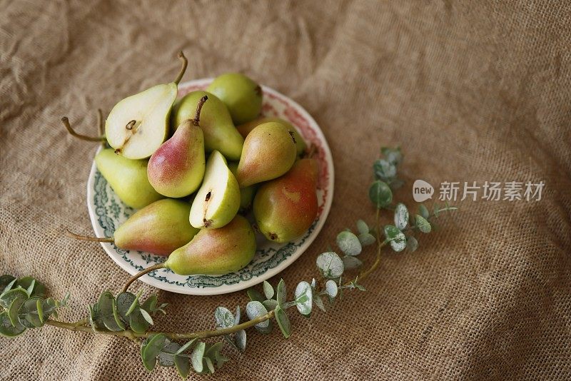 小红绿梨子，瓷盘，粗麻布上有花卉图案，树枝，夏季果实