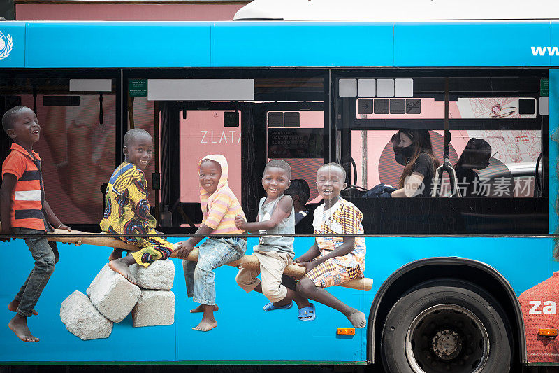 2019冠状病毒病大流行期间，一名女孩在公交车上戴着口罩，公交车上挂着联合国儿童基金会与非洲儿童合作的巨大商业广告海报。