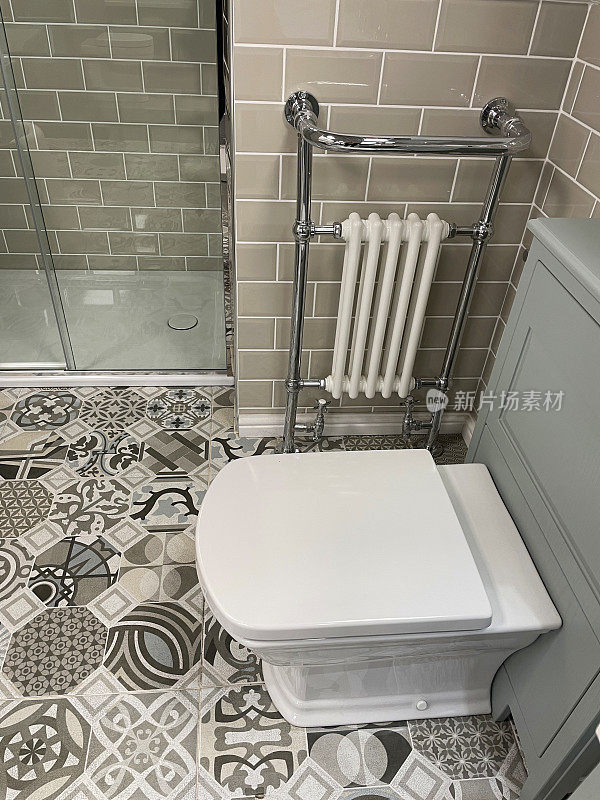 近景的现代浴室与白色，方形卫生间水箱隐藏在灰色梳妆台，铬毛巾栏杆散热器挂在墙上的光滑瓷砖，棕色瓷砖，独立淋浴间，图案地砖