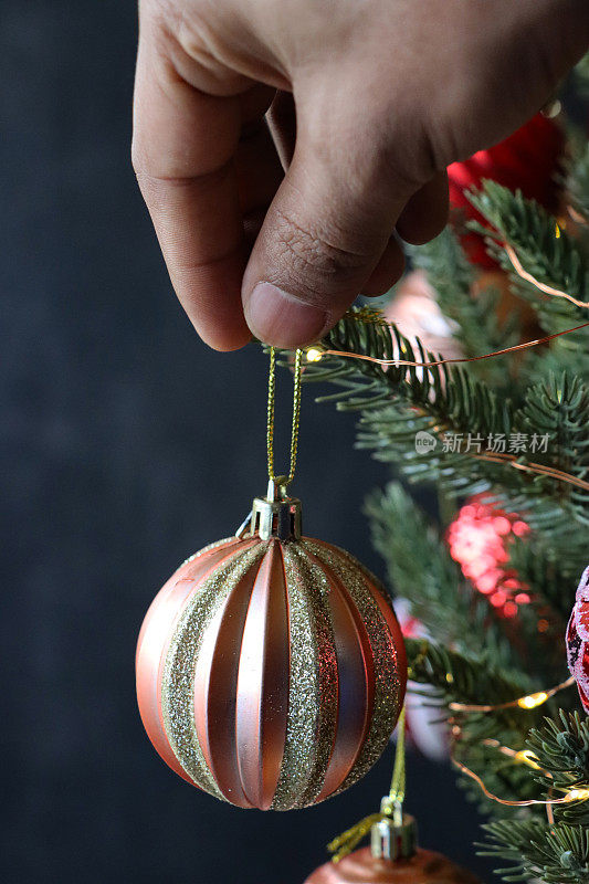 形象的无法辨认的人悬挂手风琴效应库珀和黄金闪闪发光的装饰物在人造圣诞树的树枝上，云杉针，模糊的白色神仙灯的背景，复制空间