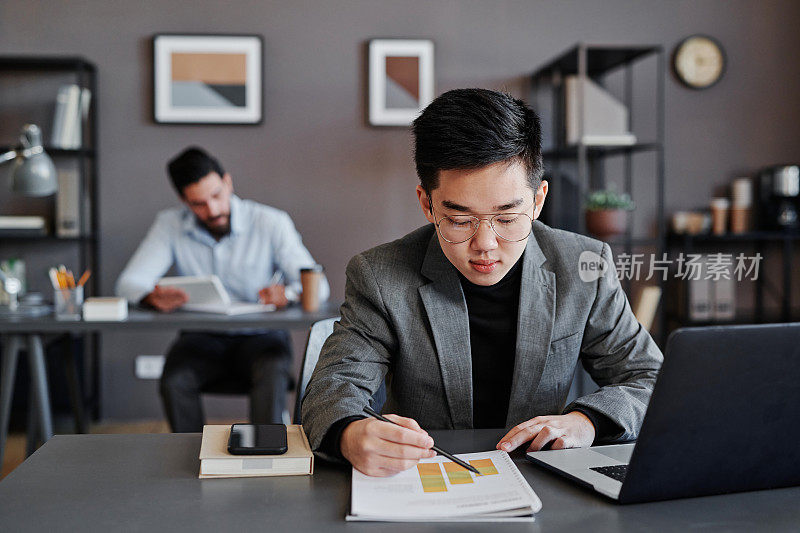 水平镜头的年轻亚洲人坐在桌子在经纪公司办公室与统计