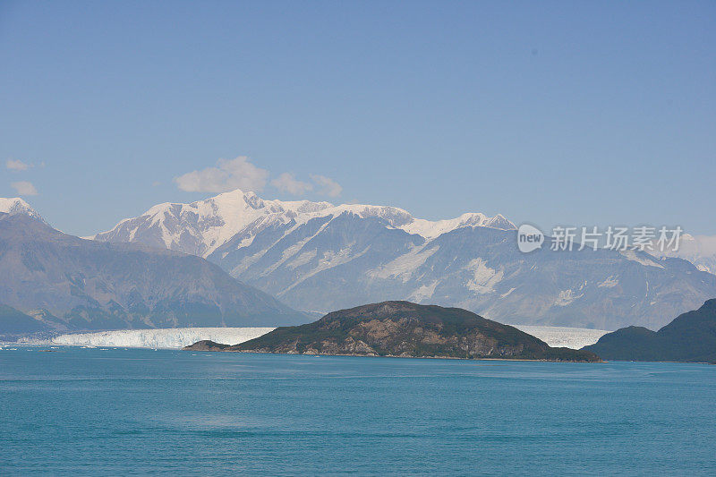 在阿拉斯加，冰川流入海洋，背景是美丽的雪山，随着全球变暖和气候变化的影响，这一景象很可能会消失。