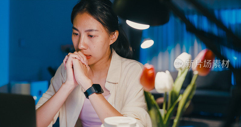 特写年轻的亚洲女性穿着正装衬衫坐在桌子前，手提电脑盯着屏幕想感到压力没有想法做紧急报告会议加班到晚上在家。