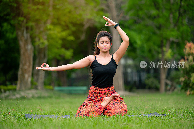 快乐的年轻女子做瑜伽伸展手和在公园室外冥想。