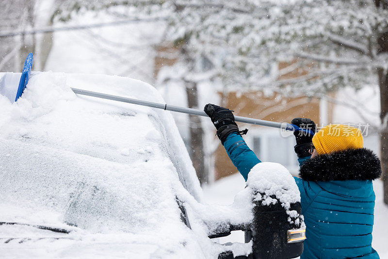 一名年轻女子在暴风雪后清理车上的积雪