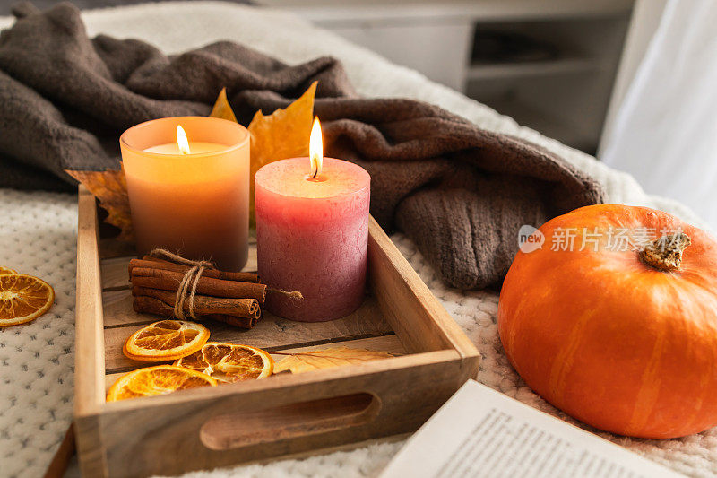 秋天的心情。点着蜡烛，端着一杯热茶，在温暖的床罩上放着一本打开的书。舒适的家居装饰