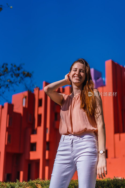 来自西班牙的年轻女子在几何红色建筑前对着镜头微笑