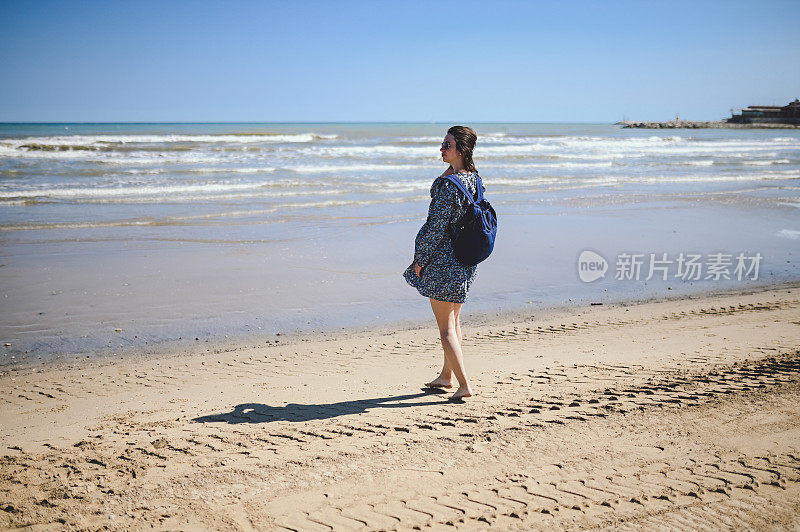 背着背包的女人赤脚走在海滩上