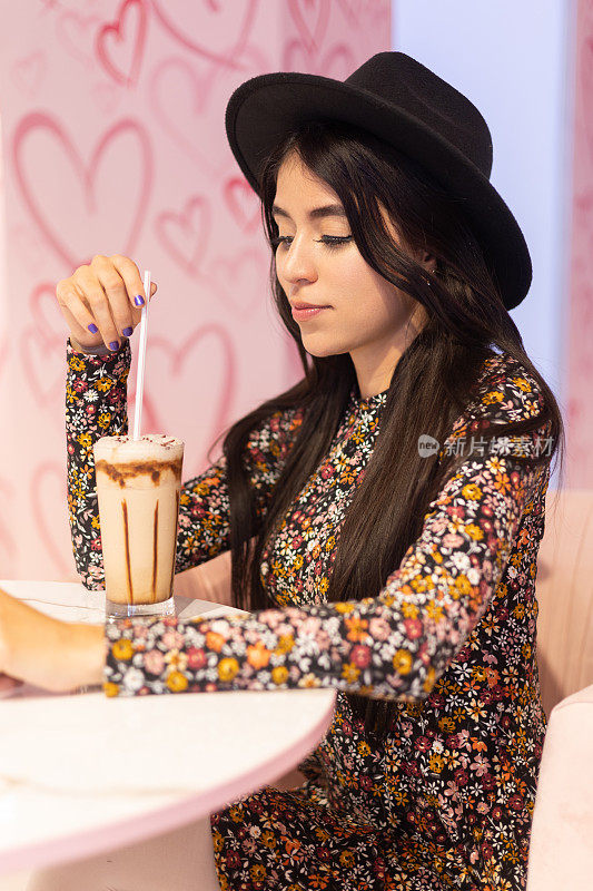 坐着的年轻女子戴着帽子和有图案的连衣裙，一杯冰巧克力饮料与冰糕