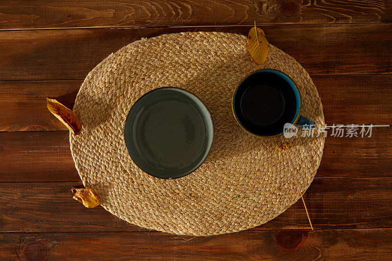 小盘子下面放柳条餐垫。木制背景上的秋叶。