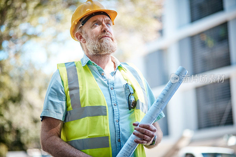 成熟的男性建筑工人抬起头，聚精会神地拿着设计图