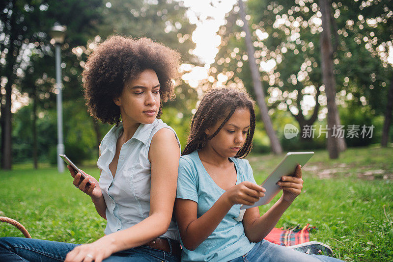 严肃的女人拿着手机，看着女儿手里的平板电脑