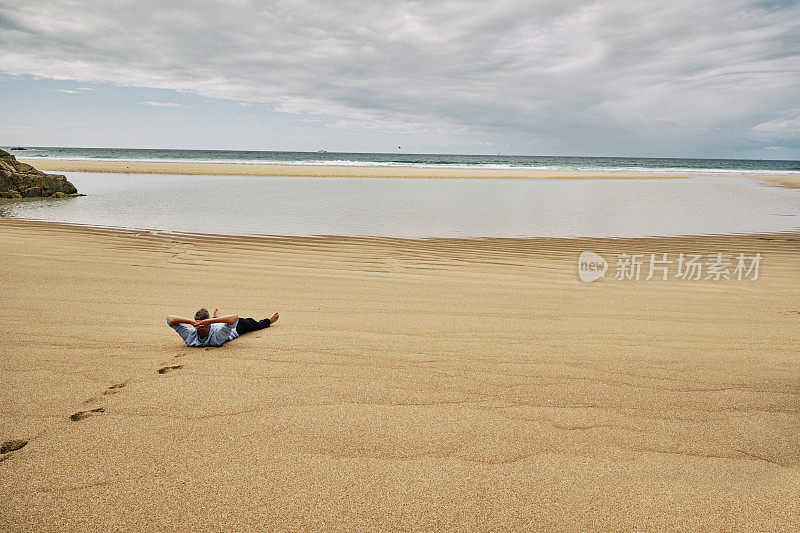 一个男人独自躺在沙滩上，双臂环抱着头，休息，远离这一切。