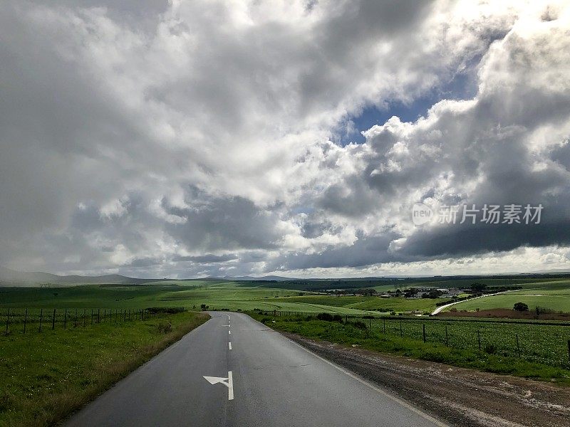这条路沿着山谷通向绿油油的农田，里面飘着白云