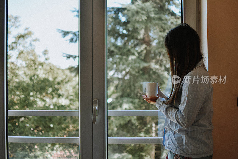 女人在窗边喝咖啡后醒来，阳光明媚的早晨。生活方式的概念