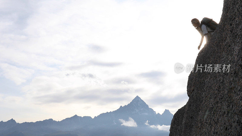 日出时，一位女登山运动员站在岩壁上眺望远方的景色