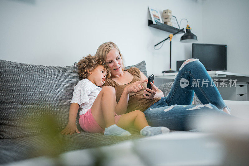 一个成熟的白人妈妈和她的女儿坐在沙发上玩着智能手机
