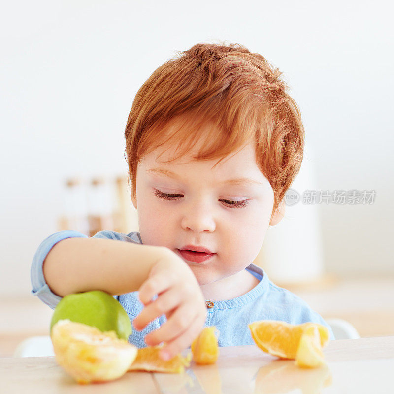 可爱的红发婴儿尝试新鲜的苹果和橙子水果