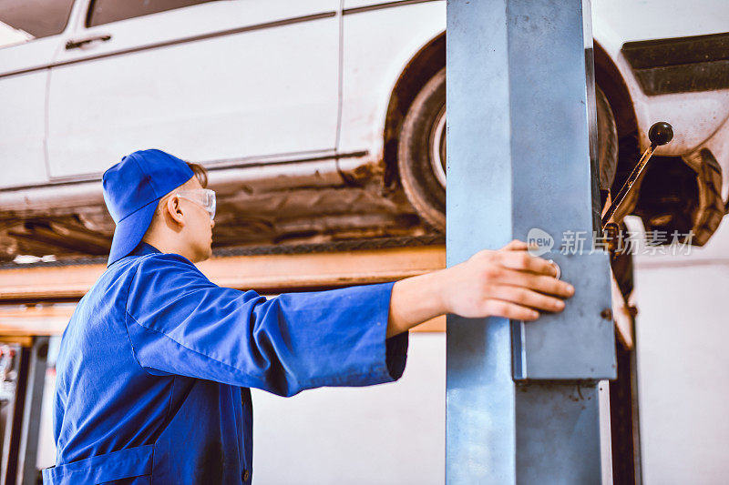 年轻男性机械师将汽车吊到机器上，以便检查排气系统