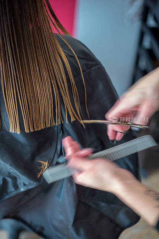 女发型师手指间握着一缕金发，梳子和剪刀特写。