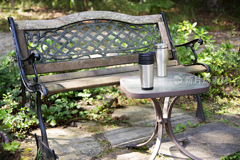 公园长椅前的桌子上放着两个可重复使用的咖啡杯。