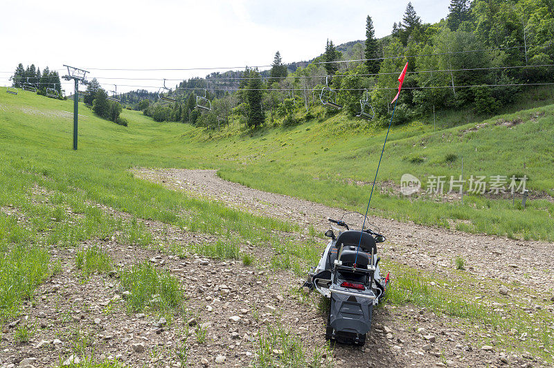 夏天，在绿山上的滑雪缆车旁边的草地和砾石上被困的雪地摩托