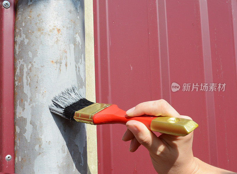 一个杂工正在用刷子刷金属栅栏柱，涂上遮蔽胶带，油漆工用的胶带以免油漆溅到栅栏上。