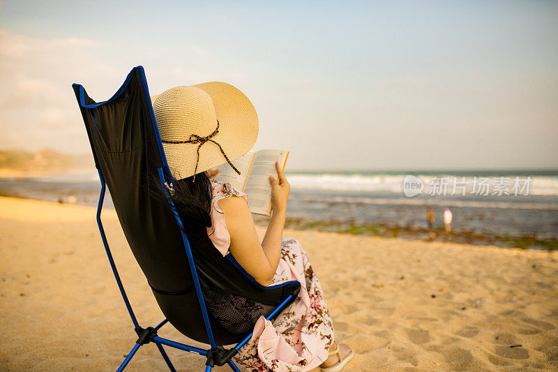 亚洲孕妇坐在沙滩上的躺椅上看书
