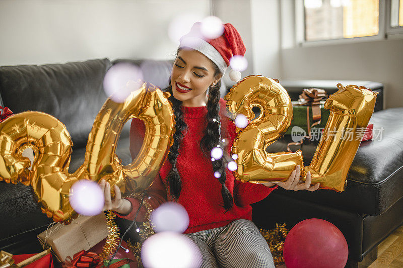 一名年轻女子在新年派对上玩得很开心，手里拿着写有“2021”的气球，代表即将到来的新年