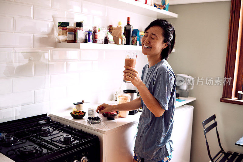 一名年轻女子在自家厨房享用自制奶昔的照片