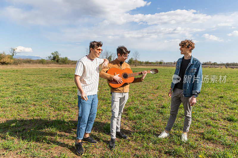 三个朋友在田野里聚在一起愉快地唱着歌，弹着吉他