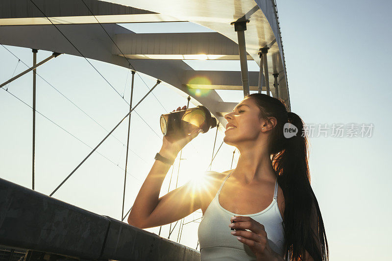 健身女子喝瓶装水。肌肉发达的年轻女性在户外锻炼后休息。