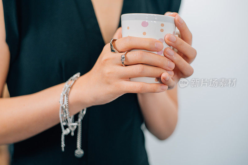 拿着咖啡的女人，手里拿着钻石戒指、银手链等奢侈品