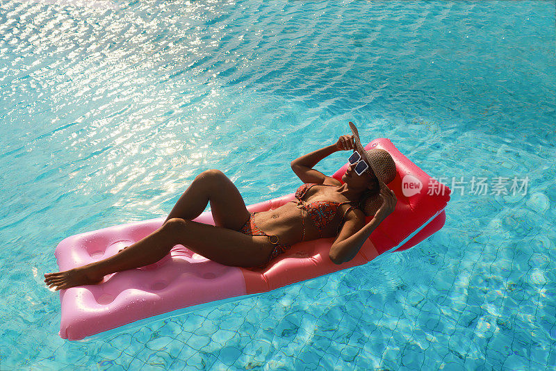 年轻的皮肤晒黑的女人在游泳池浮垫在泰国曼谷的公寓屋顶游泳池晒太阳