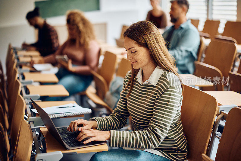 微笑的女人在大学的讲座中使用笔记本电脑。