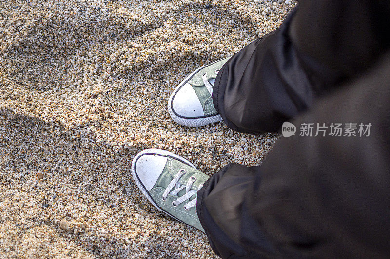 脚有问题。穿着蓝色运动鞋的女性双脚站在卵石滩上