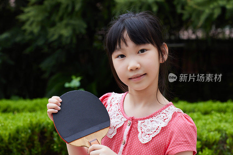 漂亮的小女孩拿着乒乓球拍，看着相机微笑