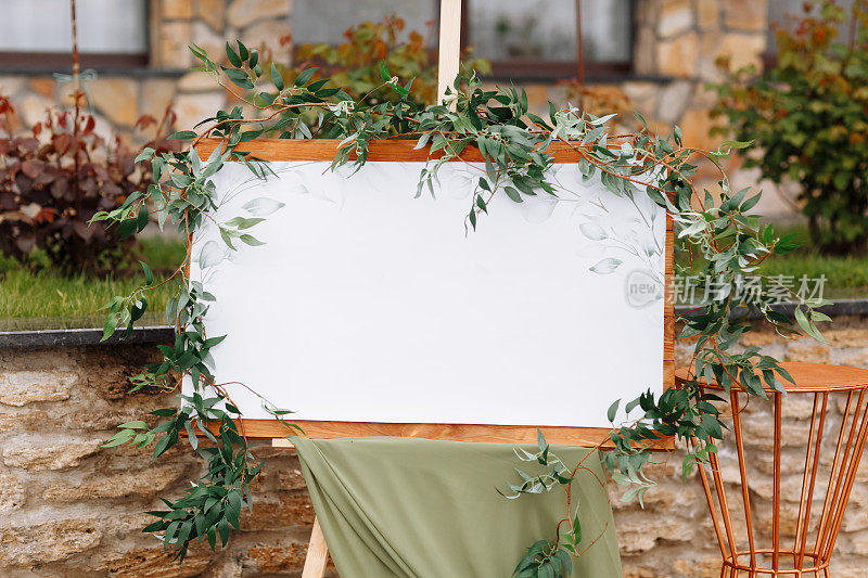 婚礼木板，模型，邀请画架，留白题字，用新鲜的绿色植物和绿色布装饰。户外婚礼帧。节日装饰，复制空间。