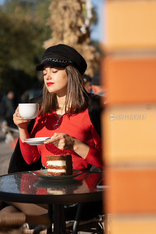 时髦的快乐女孩，长发，红唇，戴着时髦的帽子，黑色的外套，在秋天的街头咖啡馆喝咖啡。户外肖像，日光。女性秋风