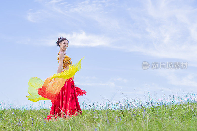 在蓝天的背景下，穿着鲜艳衣服的美女在扇子中跳着东方舞蹈