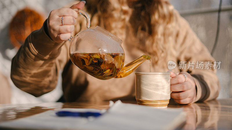 一位女士把热茶从茶壶倒进杯子里