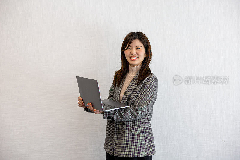 女企业家站在米色背景的肖像，拿着笔记本电脑