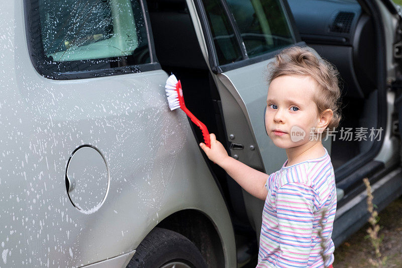 一个孩子，一个4岁的白人女孩，用刷子洗车，帮助她的父母。
